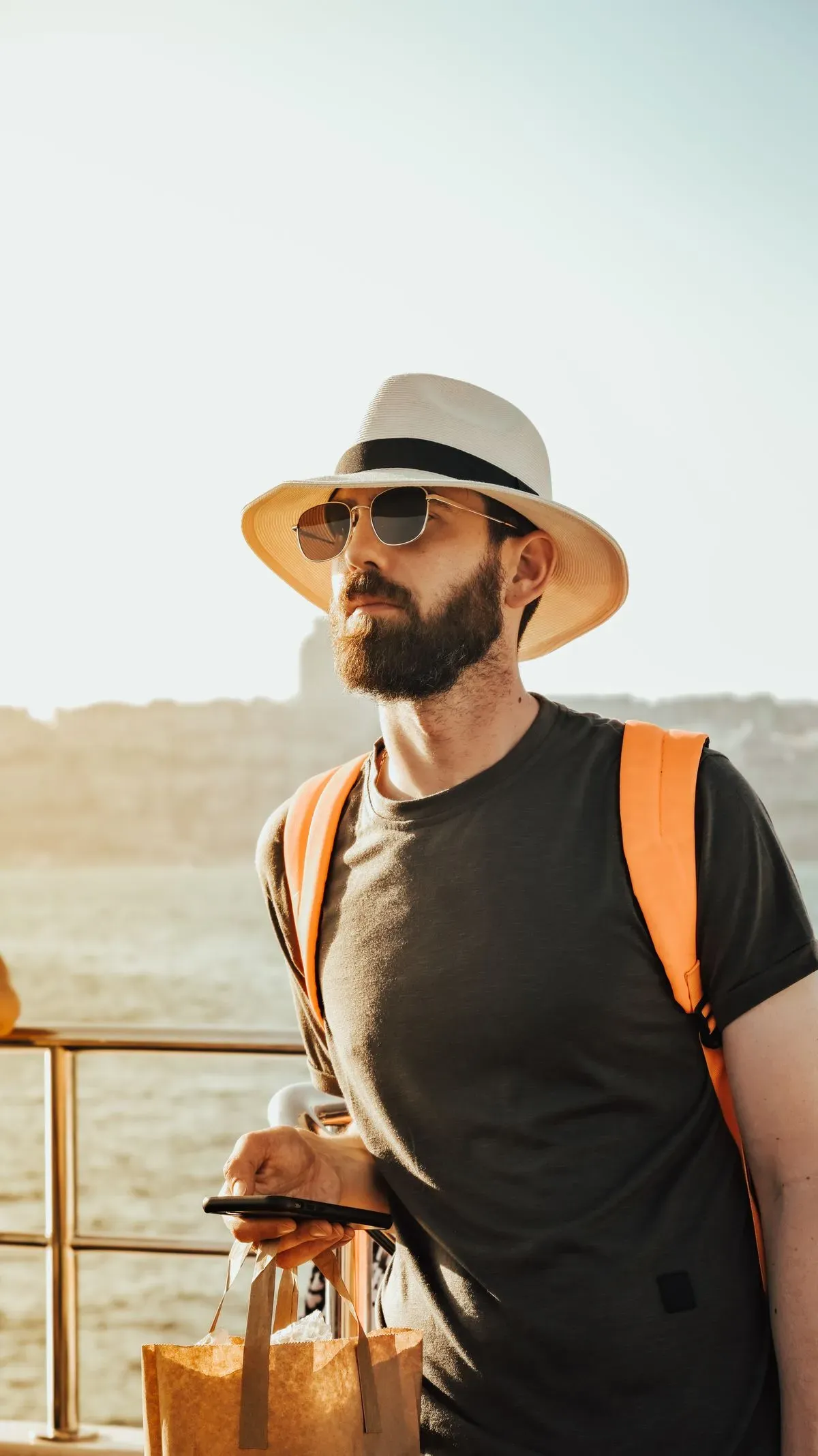A traveler wearing a hat and sunglasses by the sea